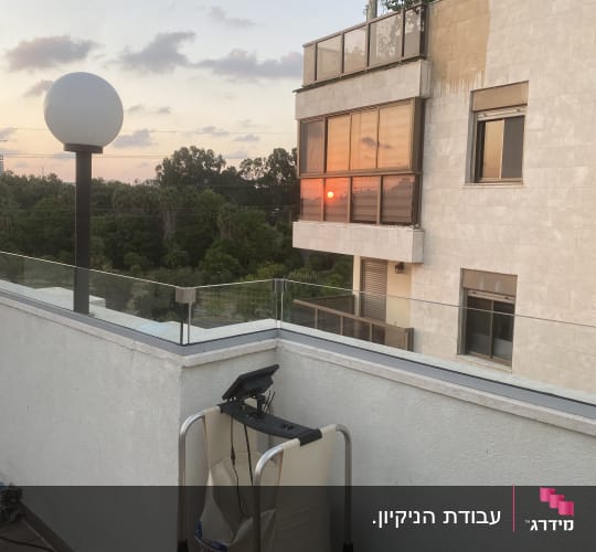 מעקה זכוכית שקוף ונקי במרפסת גג לצד ציוד ניקוי